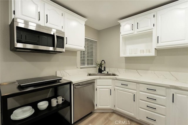 kitchen featuring white cabinets, sink, light stone countertops, light wood-type flooring, and appliances with stainless steel finishes