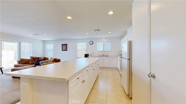 kitchen with light carpet, a center island, white cabinetry, and a healthy amount of sunlight