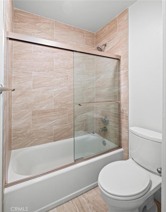 bathroom with hardwood / wood-style floors, toilet, and combined bath / shower with glass door