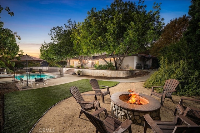 patio terrace at dusk featuring a fenced in pool, a yard, and an outdoor fire pit