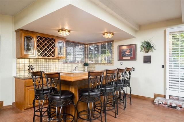 bar featuring light hardwood / wood-style floors, sink, and backsplash