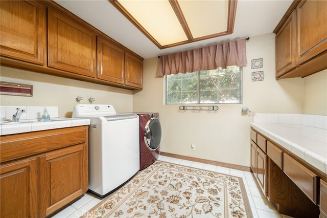 clothes washing area with light tile patterned flooring, cabinets, and washing machine and dryer