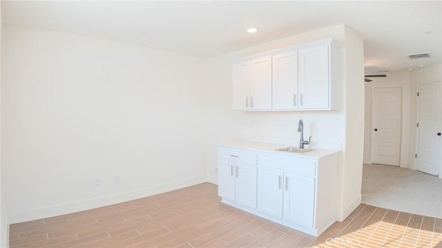 bar with white cabinetry, sink, and light wood-type flooring