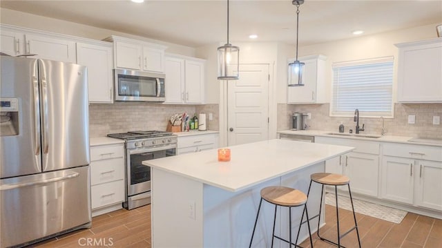 kitchen with sink, appliances with stainless steel finishes, a kitchen island, pendant lighting, and white cabinets