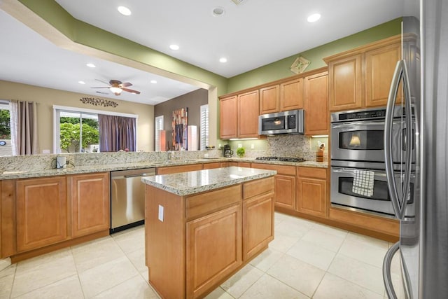 kitchen with kitchen peninsula, appliances with stainless steel finishes, light stone countertops, ceiling fan, and a kitchen island