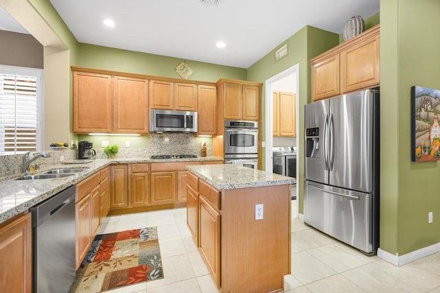 kitchen featuring appliances with stainless steel finishes, light stone counters, a kitchen island, and sink