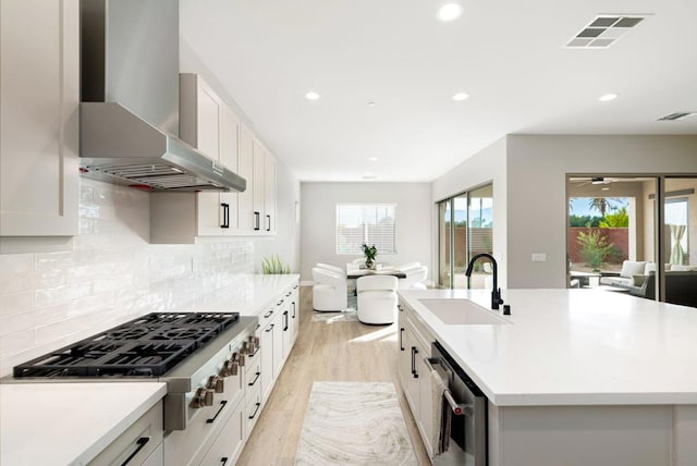 kitchen with white cabinetry, an island with sink, appliances with stainless steel finishes, wall chimney exhaust hood, and sink