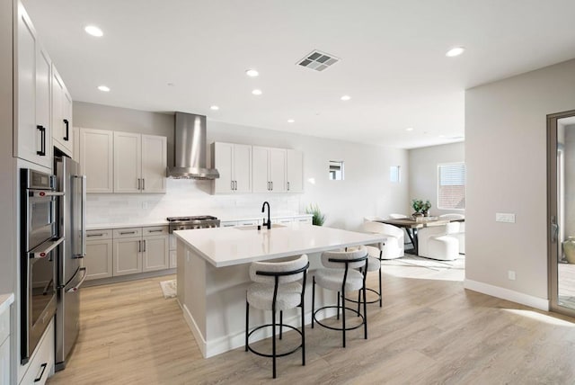 kitchen featuring range hood, a breakfast bar, sink, light hardwood / wood-style flooring, and an island with sink