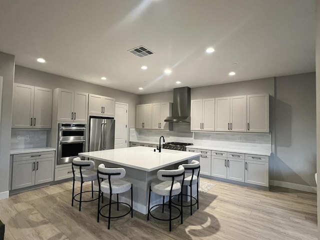 kitchen featuring tasteful backsplash, wall chimney range hood, a breakfast bar, appliances with stainless steel finishes, and an island with sink