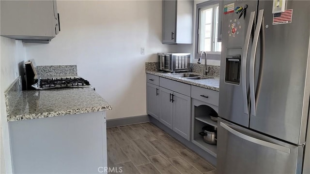 kitchen featuring light stone countertops, appliances with stainless steel finishes, sink, gray cabinets, and light hardwood / wood-style floors