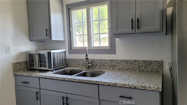 kitchen featuring gray cabinets, light stone counters, and sink