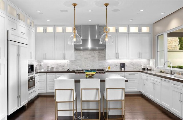 51 Monarch Beach Resort S, Dana Point, CA 92629 - kitchen featuring wall chimney exhaust hood, built in appliances, a kitchen island, backsplash, and white cabinetry