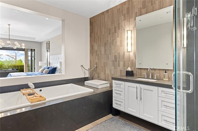 bathroom featuring an inviting chandelier, wood-type flooring, shower with separate bathtub, vanity, and tile walls