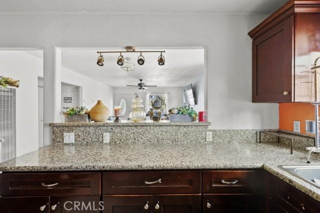 kitchen featuring ceiling fan, light stone countertops, sink, and kitchen peninsula