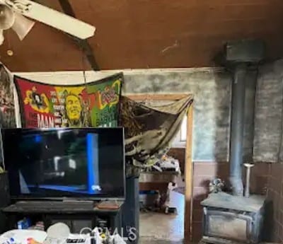 misc room with ceiling fan, a wood stove, and concrete flooring