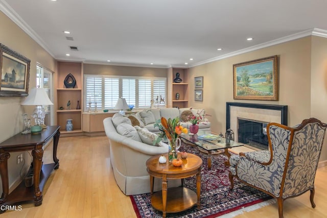 living room with crown molding, built in features, light wood-type flooring, and a tile fireplace