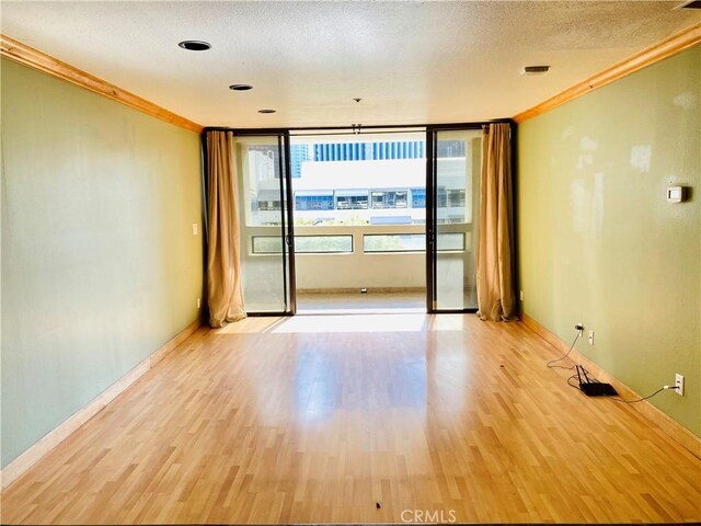 unfurnished room featuring a textured ceiling, light wood-type flooring, and crown molding