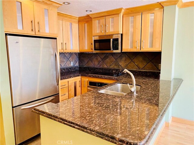 kitchen with dark stone countertops, kitchen peninsula, sink, and appliances with stainless steel finishes