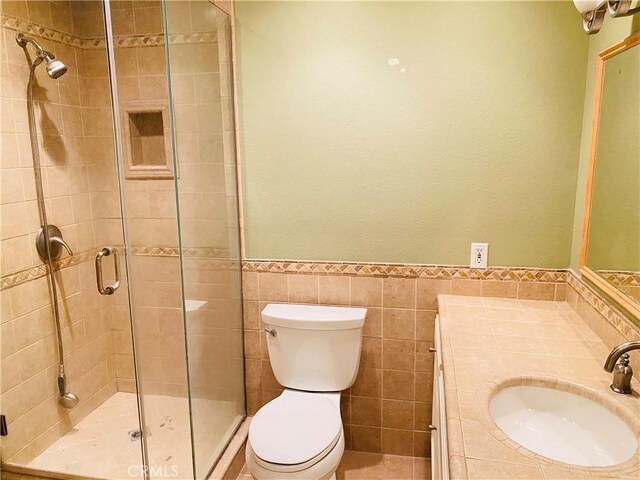 bathroom featuring a shower with door, vanity, tile walls, and toilet