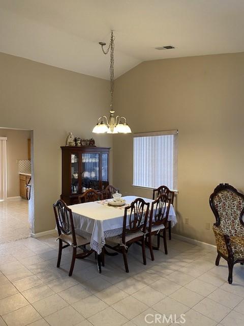 tiled dining area featuring a chandelier and vaulted ceiling