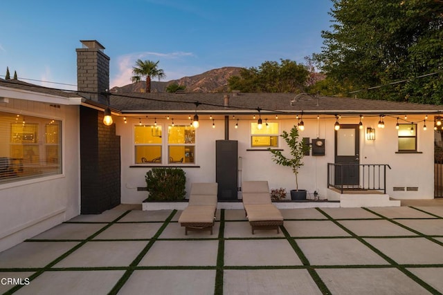 back house at dusk featuring a mountain view and a patio