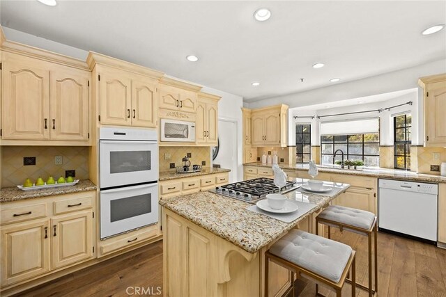 kitchen with tasteful backsplash, white appliances, a kitchen breakfast bar, dark wood-type flooring, and a center island