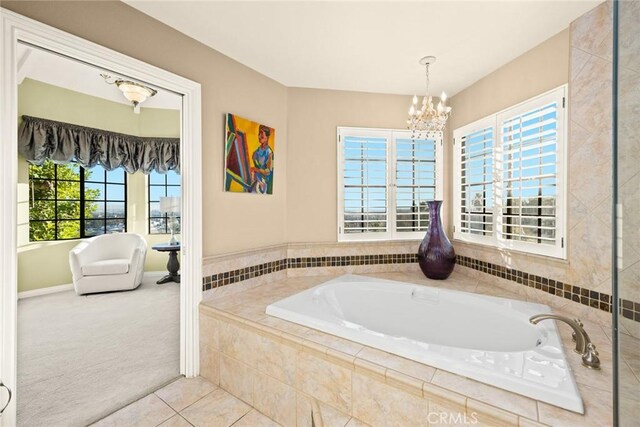 bathroom with a chandelier, tile patterned floors, and tiled tub