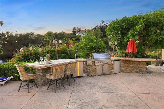 patio terrace at dusk with an outdoor bar and area for grilling