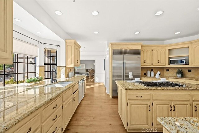 kitchen with light stone countertops, light brown cabinets, stainless steel appliances, sink, and light wood-type flooring