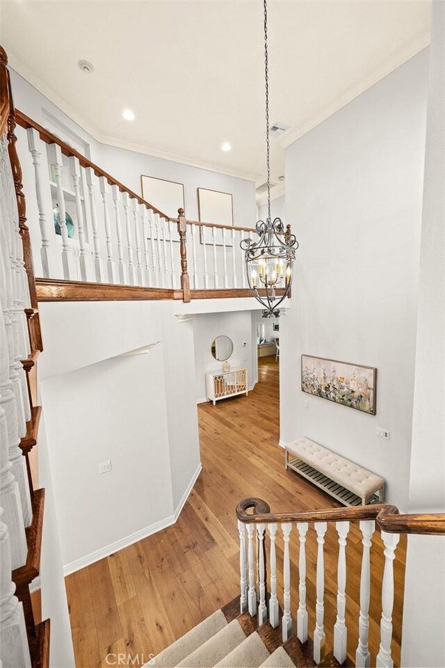 staircase featuring hardwood / wood-style flooring, ornamental molding, and a chandelier