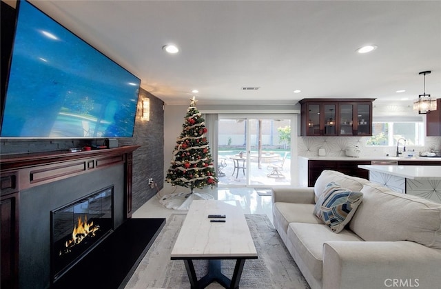 living room with crown molding, sink, a healthy amount of sunlight, and light wood-type flooring