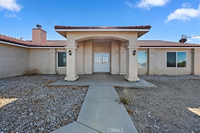 view of exterior entry with stucco siding, a tiled roof, a chimney, and french doors