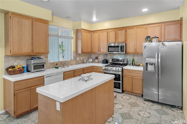 kitchen featuring appliances with stainless steel finishes, backsplash, light brown cabinets, tile countertops, and a center island