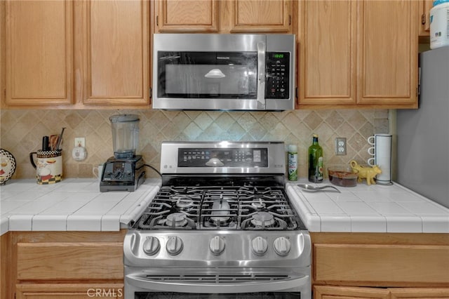 kitchen with tile countertops, light brown cabinets, backsplash, and appliances with stainless steel finishes