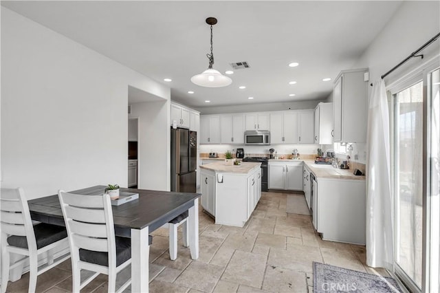 kitchen featuring sink, appliances with stainless steel finishes, white cabinetry, a kitchen island, and decorative light fixtures