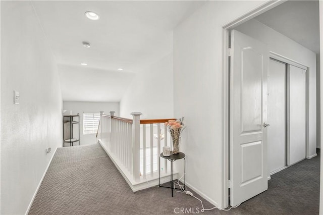 hall with vaulted ceiling and dark colored carpet