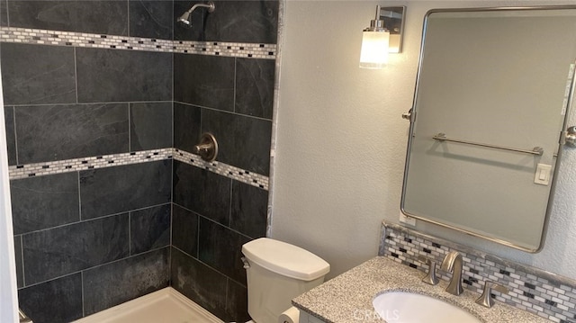 bathroom with a tile shower, decorative backsplash, vanity, and toilet