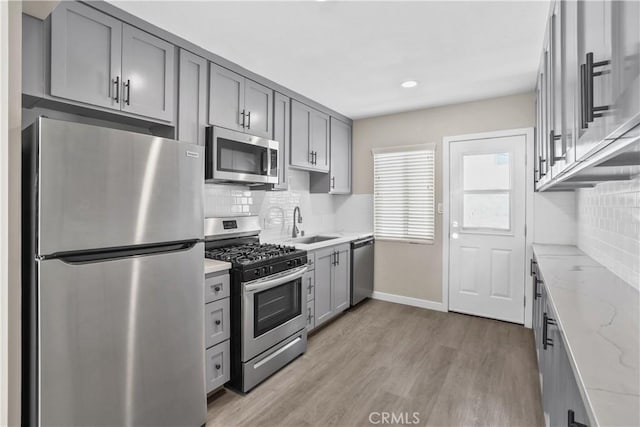 kitchen with decorative backsplash, gray cabinets, light stone countertops, and appliances with stainless steel finishes