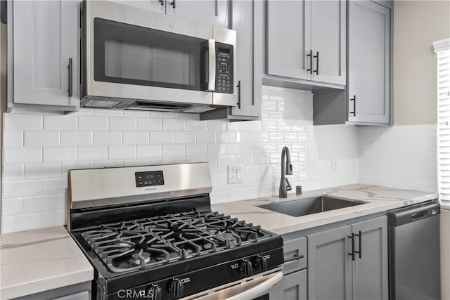 kitchen with backsplash, stainless steel appliances, gray cabinets, and sink