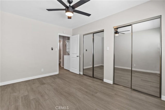 unfurnished bedroom with light hardwood / wood-style floors, ceiling fan, and multiple closets