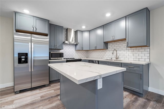 kitchen featuring sink, wall chimney range hood, appliances with stainless steel finishes, a kitchen island, and hardwood / wood-style flooring