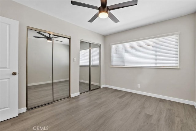 unfurnished bedroom with ceiling fan, light wood-type flooring, and multiple closets