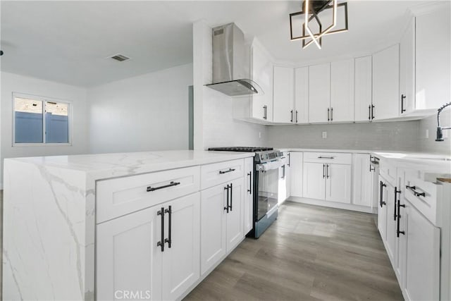 kitchen with gas range, wall chimney range hood, decorative light fixtures, light hardwood / wood-style flooring, and white cabinets