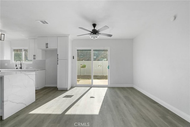 kitchen featuring white cabinets, hardwood / wood-style flooring, decorative backsplash, ceiling fan, and light stone countertops