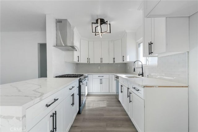 kitchen with white cabinets, wall chimney exhaust hood, light hardwood / wood-style floors, light stone counters, and stainless steel appliances