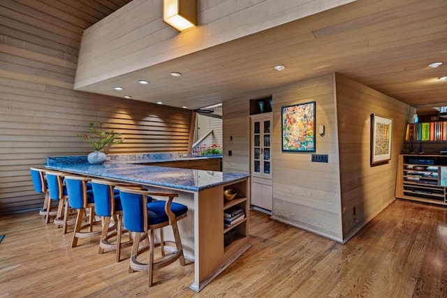 bar with dark stone counters, light hardwood / wood-style flooring, wooden walls, and wood ceiling