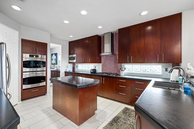 kitchen featuring wall chimney exhaust hood, sink, appliances with stainless steel finishes, a kitchen island, and decorative backsplash