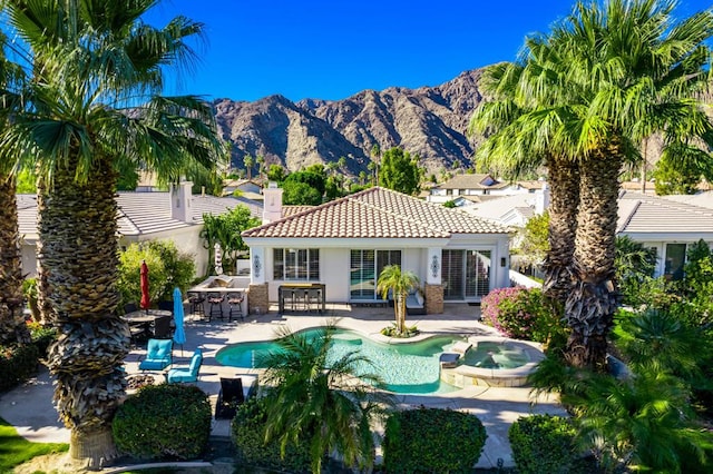 back of house with a swimming pool with hot tub, exterior bar, a mountain view, and a patio area