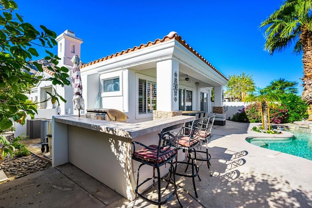 view of patio / terrace featuring a fenced in pool, an outdoor bar, ceiling fan, and an outdoor kitchen