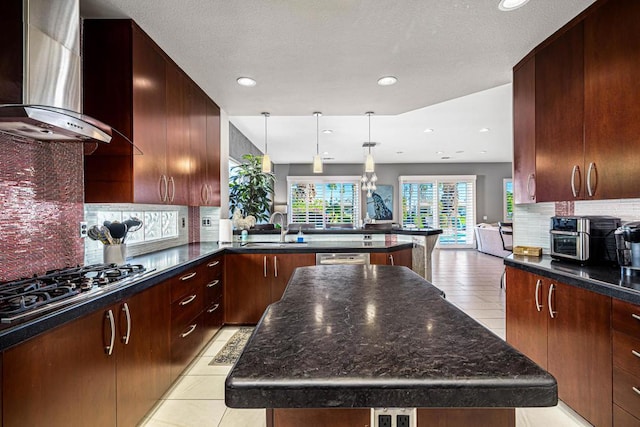 kitchen with a kitchen island, stainless steel gas stovetop, sink, hanging light fixtures, and wall chimney range hood